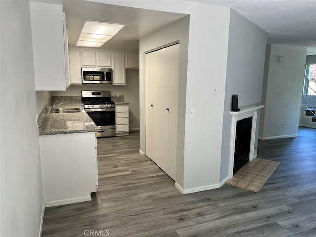 kitchen featuring hardwood / wood-style flooring, stainless steel appliances, dark stone countertops, and white cabinetry