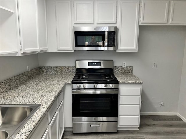 kitchen featuring light stone countertops, appliances with stainless steel finishes, white cabinetry, dark hardwood / wood-style flooring, and sink