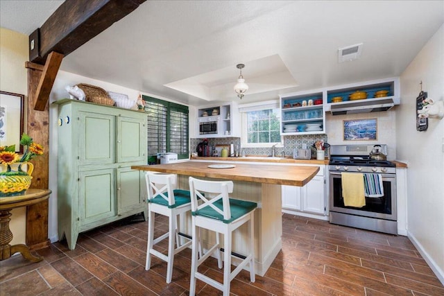 kitchen featuring a raised ceiling, a breakfast bar, hanging light fixtures, wood counters, and stainless steel range