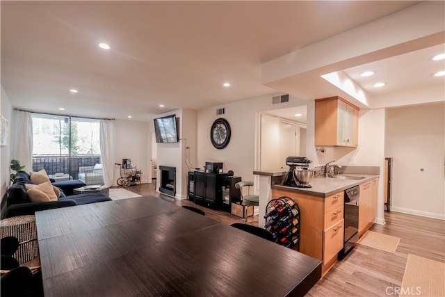 kitchen featuring black dishwasher, light hardwood / wood-style floors, sink, kitchen peninsula, and light brown cabinets