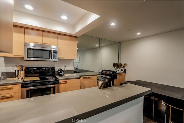 kitchen featuring kitchen peninsula, light brown cabinets, and appliances with stainless steel finishes