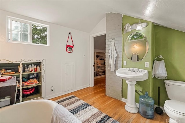 interior space with toilet, hardwood / wood-style floors, vaulted ceiling, and a washtub