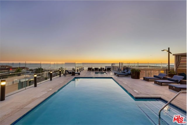 pool at dusk featuring a patio and a water view