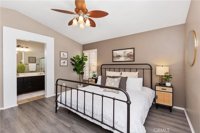 bedroom featuring dark hardwood / wood-style floors, ceiling fan, connected bathroom, and vaulted ceiling