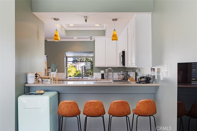 kitchen with crown molding, a tray ceiling, hanging light fixtures, and a breakfast bar area