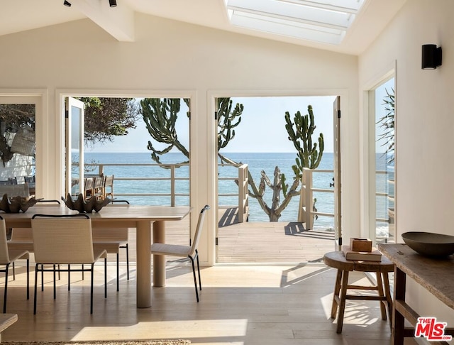 dining area featuring hardwood / wood-style flooring, vaulted ceiling with skylight, a water view, and a wealth of natural light