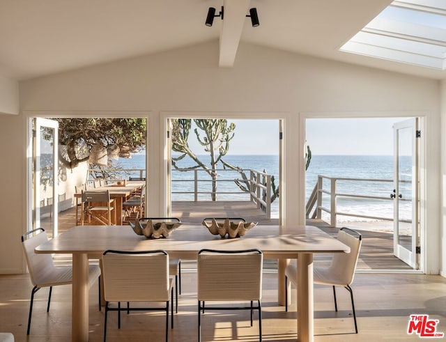 dining space featuring wood-type flooring, a water view, plenty of natural light, and lofted ceiling with skylight