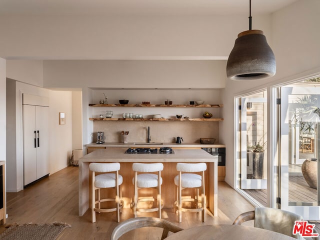 kitchen featuring light wood-type flooring, paneled built in fridge, hanging light fixtures, and a breakfast bar area