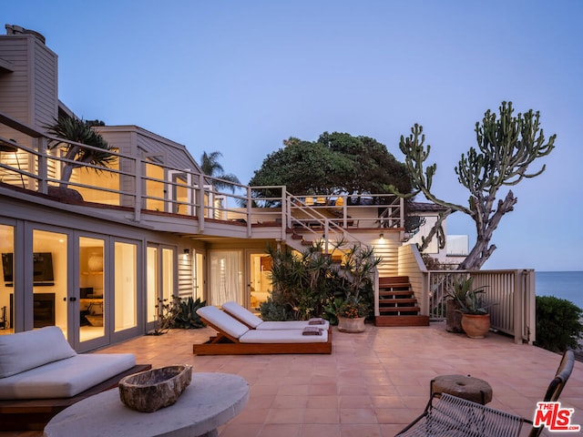 patio terrace at dusk featuring french doors, a fire pit, and a water view