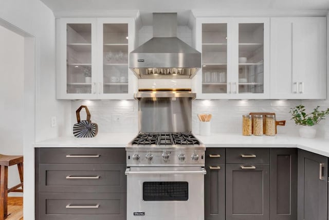 kitchen featuring white cabinetry, wall chimney exhaust hood, hardwood / wood-style floors, decorative backsplash, and stainless steel stove