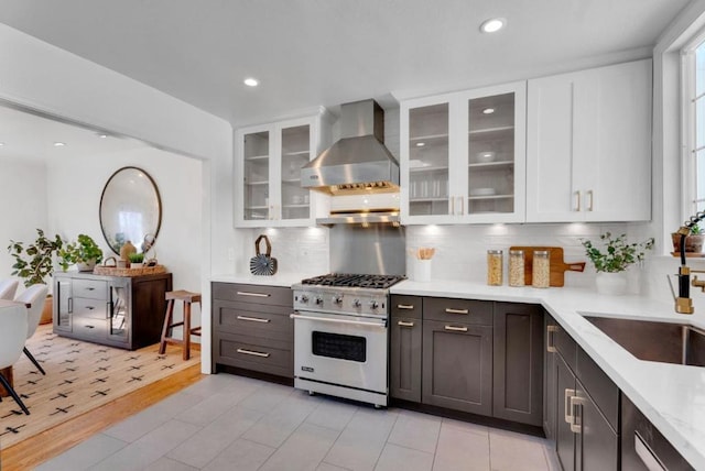 kitchen featuring wall chimney exhaust hood, high end stove, backsplash, white cabinets, and light wood-type flooring