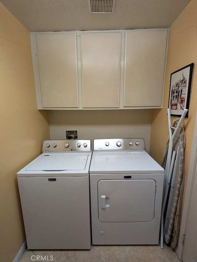 laundry area featuring washer and clothes dryer, light tile patterned flooring, cabinets, and a textured ceiling