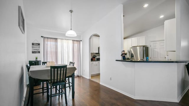 kitchen with lofted ceiling, white cabinets, hanging light fixtures, dark hardwood / wood-style floors, and stainless steel fridge