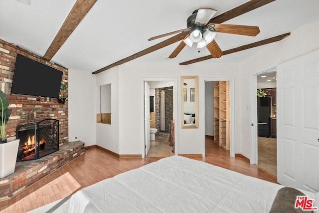 bedroom featuring a walk in closet, a fireplace, light hardwood / wood-style floors, ceiling fan, and ensuite bathroom