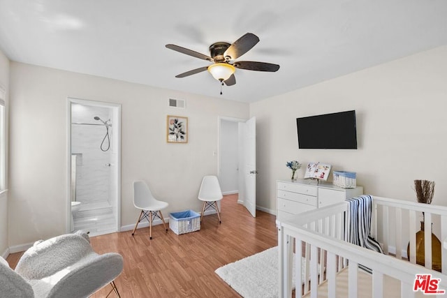 bedroom featuring ceiling fan, light hardwood / wood-style floors, ensuite bath, and a crib