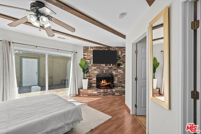 bedroom with ceiling fan, a fireplace, light hardwood / wood-style flooring, and vaulted ceiling with beams