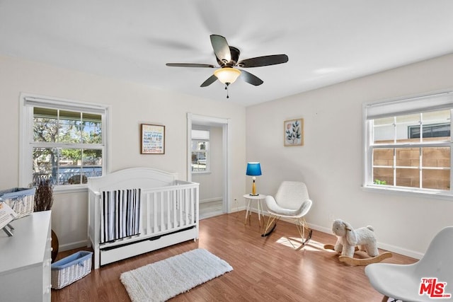 bedroom featuring ceiling fan, dark hardwood / wood-style flooring, and a crib