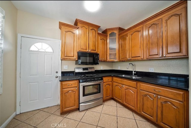 kitchen featuring stainless steel gas stove, light tile patterned floors, dark stone counters, and sink