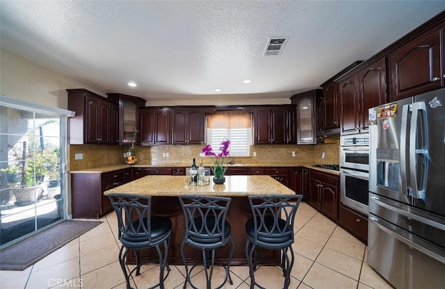 kitchen with decorative backsplash, a kitchen breakfast bar, dark brown cabinets, stainless steel appliances, and a center island