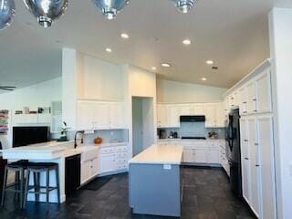 kitchen featuring lofted ceiling, a kitchen island, white cabinetry, a kitchen breakfast bar, and black refrigerator