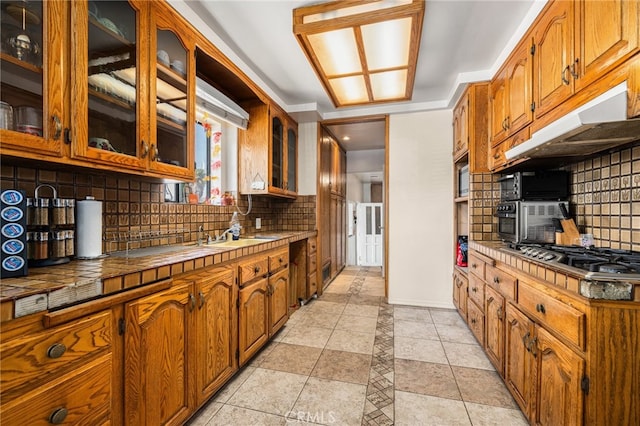 kitchen with light tile patterned flooring, sink, backsplash, stainless steel gas stovetop, and tile counters