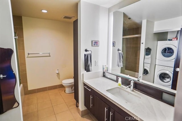 bathroom with a tile shower, tile patterned floors, stacked washer / dryer, toilet, and vanity