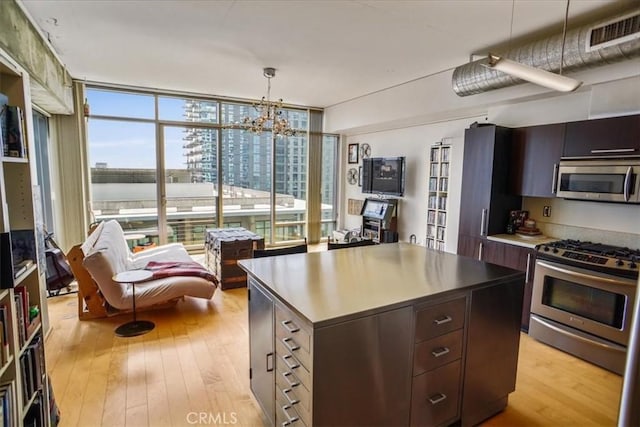 kitchen featuring dark brown cabinetry, pendant lighting, light hardwood / wood-style floors, a kitchen island, and appliances with stainless steel finishes