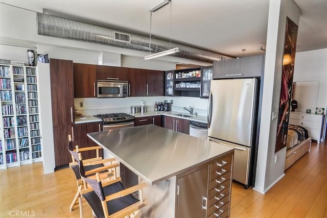 1100 S Hope St Unit 1507, Los Angeles, CA 90015 - kitchen featuring appliances with stainless steel finishes, a sink, a breakfast bar area, open shelves, and light wood finished floors