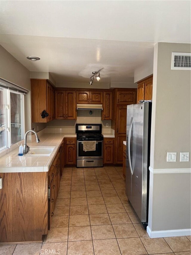 kitchen featuring sink, tile counters, light tile patterned floors, and appliances with stainless steel finishes