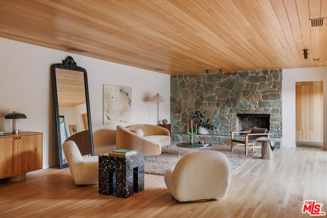 living room with hardwood / wood-style flooring, a stone fireplace, and wooden ceiling