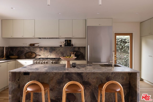 kitchen with sink, dark stone countertops, light wood-type flooring, and stainless steel appliances