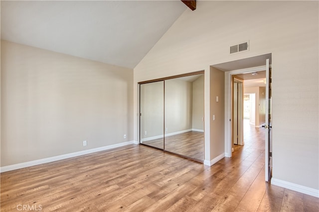 unfurnished bedroom featuring a closet, light wood-type flooring, beam ceiling, and high vaulted ceiling