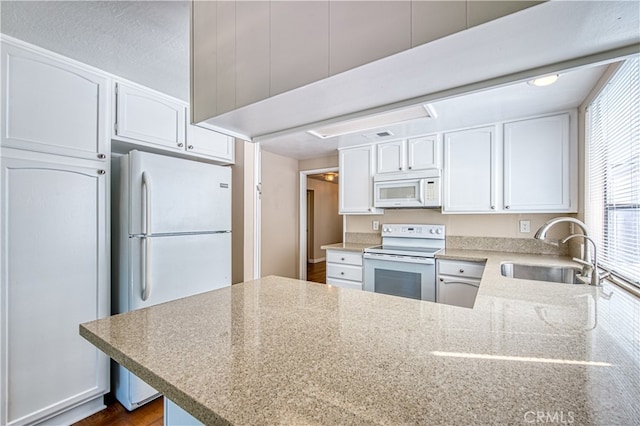 kitchen with white appliances, kitchen peninsula, white cabinetry, and sink