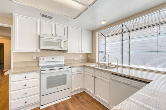 kitchen with a textured ceiling, hardwood / wood-style flooring, sink, white cabinets, and white appliances