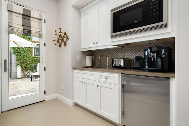 bar with decorative backsplash, stainless steel appliances, white cabinetry, and sink