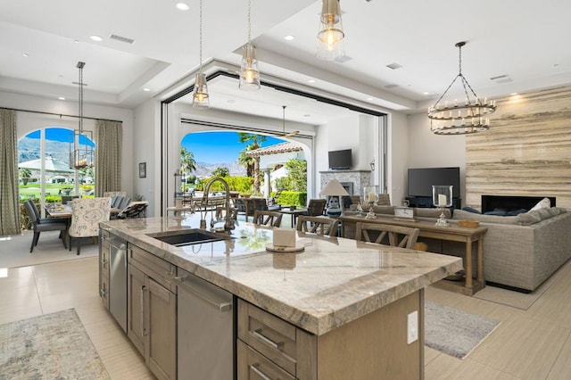 kitchen with pendant lighting, sink, light stone countertops, and an island with sink