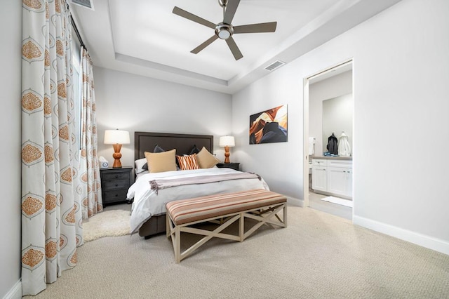 carpeted bedroom with ceiling fan, a raised ceiling, and connected bathroom