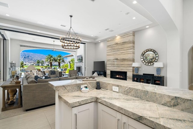 kitchen featuring light stone counters, a large fireplace, pendant lighting, a notable chandelier, and white cabinets