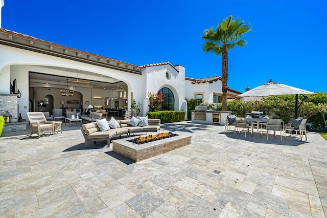 view of patio / terrace featuring an outdoor kitchen, a grill, ceiling fan, and an outdoor living space with a fire pit