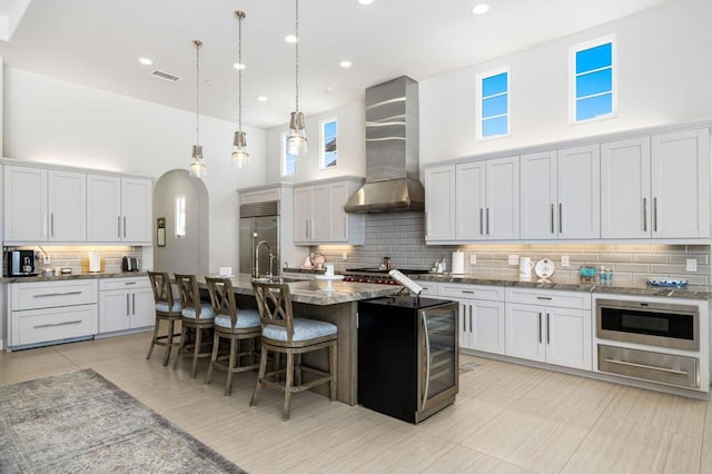 kitchen with a center island with sink, white cabinets, wall chimney range hood, and a towering ceiling