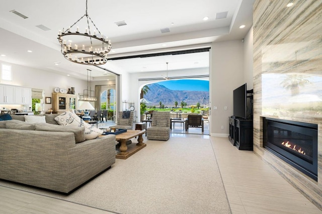 tiled living room featuring a fireplace, a towering ceiling, an inviting chandelier, and a raised ceiling