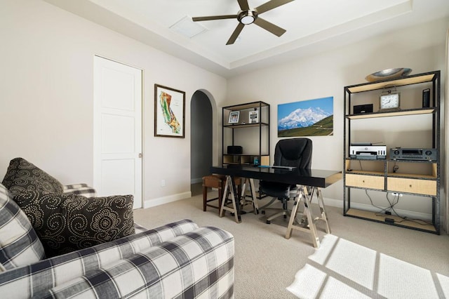 carpeted home office with ceiling fan and a tray ceiling