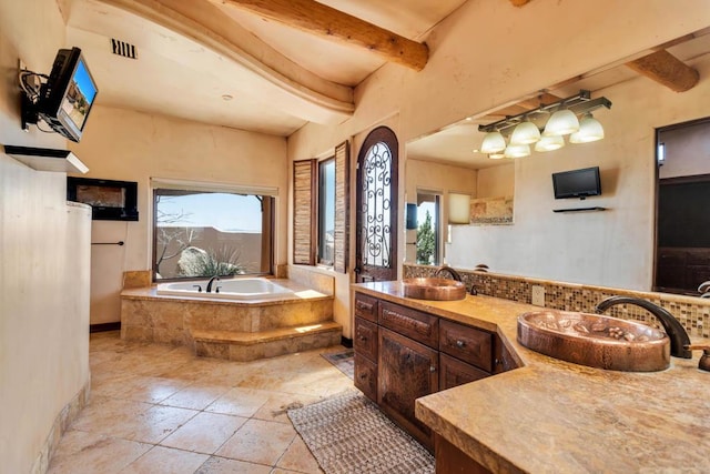 bathroom featuring beamed ceiling, vanity, and tiled tub