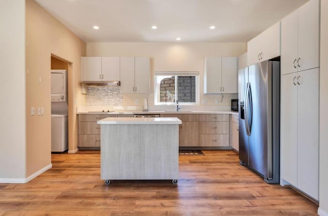 kitchen featuring white cabinetry, sink, light hardwood / wood-style flooring, stacked washer / drying machine, and black appliances