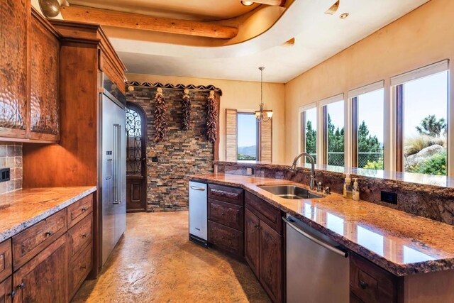 kitchen with sink, light stone countertops, decorative light fixtures, stainless steel appliances, and a chandelier