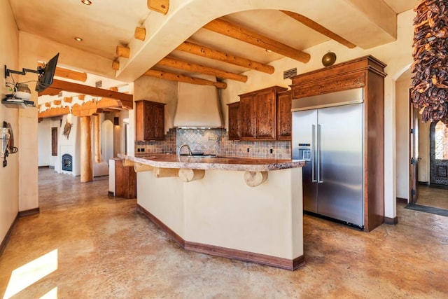 kitchen featuring a kitchen bar, tasteful backsplash, custom range hood, beam ceiling, and built in refrigerator