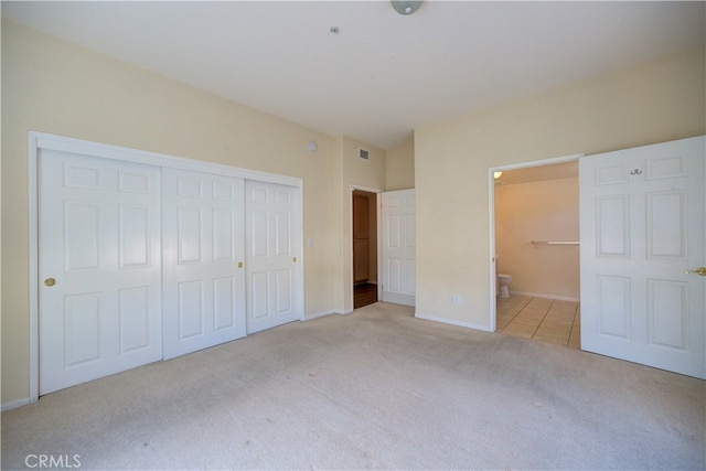 unfurnished bedroom featuring light carpet, a closet, and ensuite bathroom