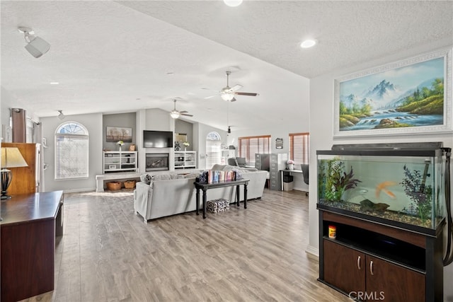 living room with light hardwood / wood-style flooring, vaulted ceiling, ceiling fan, and a textured ceiling