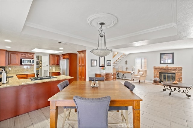 dining room featuring a textured ceiling, a raised ceiling, a fireplace, and crown molding