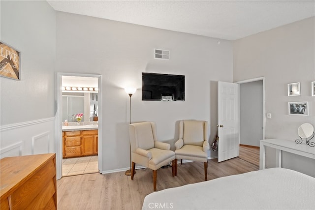 bedroom with connected bathroom, a high ceiling, and light wood-type flooring